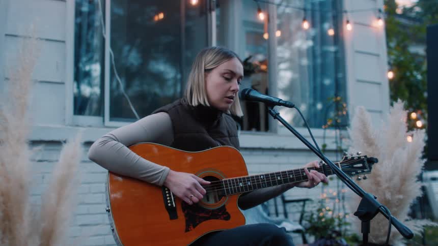 A young woman singing and playing guitar on a back yard