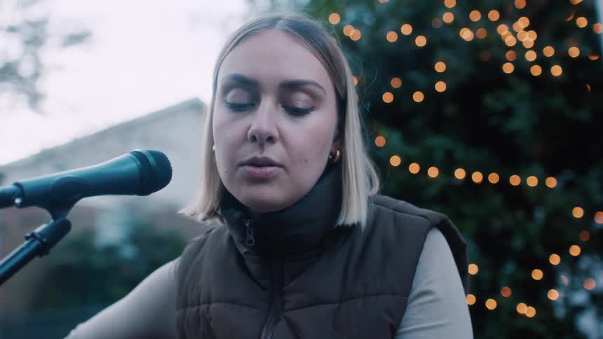 A young woman sings and plays acoustic guitar