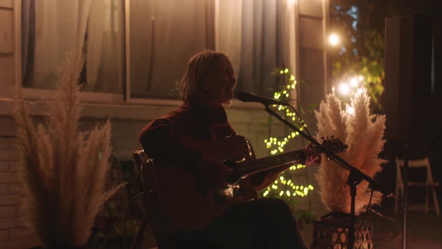 Woman singing and playing the guitar outside the house at night