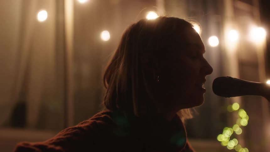 Closeup of a woman singing into a microphone with warm bokeh lights in the background