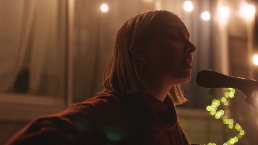 Closeup of a woman singing into a microphone with warm bokeh lights in the background