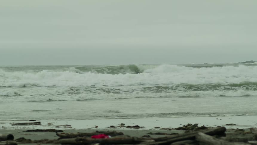 Waves crash toward the beach on a gloomy day with a lone beach toy resting in the sand