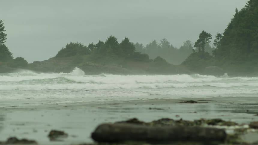 Multiple waves break and wash upon a sandy beach on an overcast day