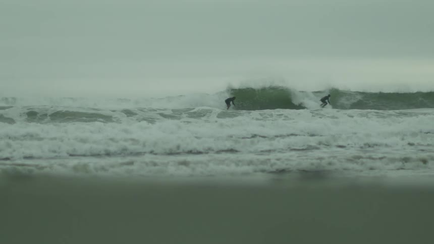 People surfing the waves near the coast on a cloudy day