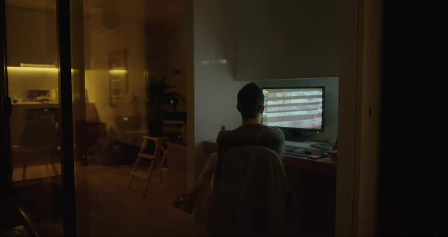 A man is working from home at his computer to the right of his kitchen and he moves his computer mouse as he works