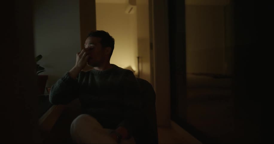 Man sitting in a dark room with a hand on his worried face