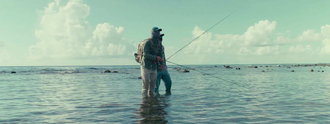 Two fishermen wearing jackets stand in water and fish on a cloudy day