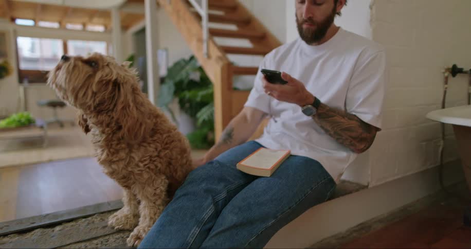 Portrait of a man sitting using his cellphone and petting his dog beside him