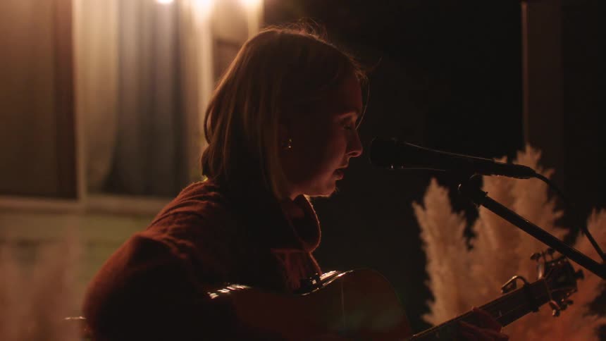 A young blonde woman plays the guitar and sings into a microphone