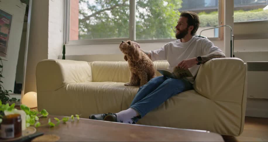Man reading in the couch plays with his pet dog