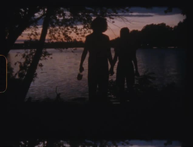 The silhouettes of two people holding hands in front of a lake on a dark morning