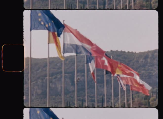 Flags of various countries placed side by side in an outdoor setting with mountains on the horizon