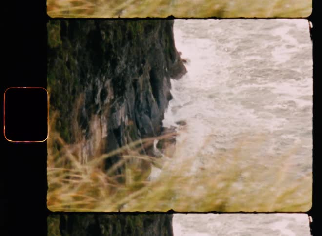 An elevated view of turbulent ocean waters churning at the base of a rocky cliff in the daytime