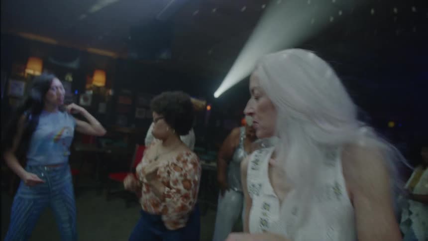 Grayhaired woman dancing in a nightclub with several people around having fun