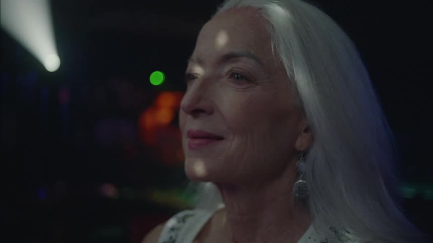 Elderly woman dancing among other people in a party at night