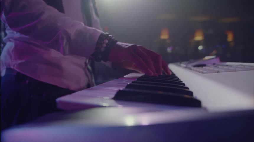 A man stands while playing a electric keyboard under a spotlight