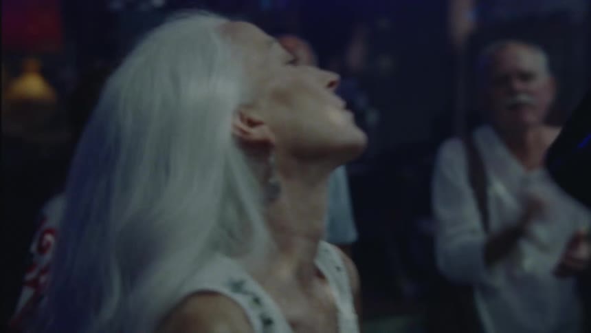 Grayhaired woman dancing in a crowded nightclub having fun and then suddenly stopping and closing her eyes