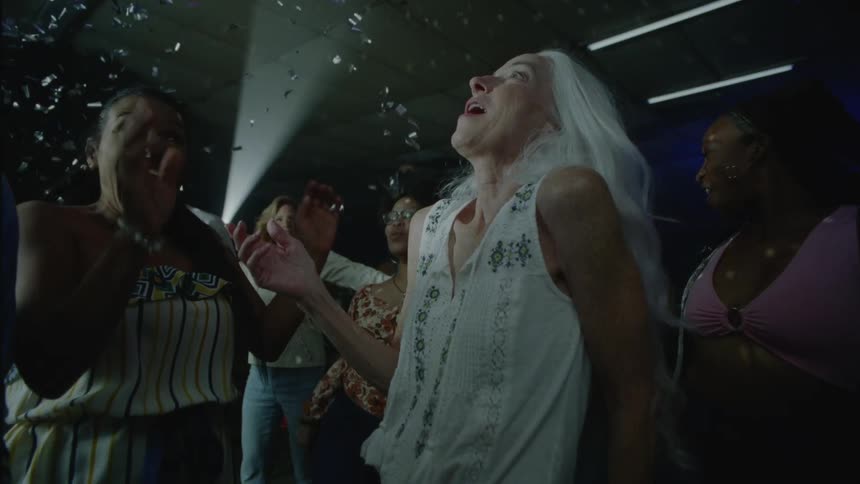 Friends dancing at party smile as silver confetti drops