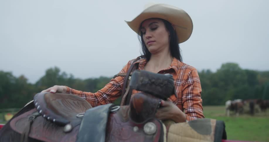 A woman carrying horse saddles outdoors