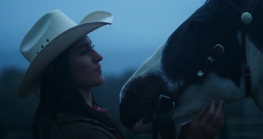 A woman and a horse outdoors in the rain at dusk