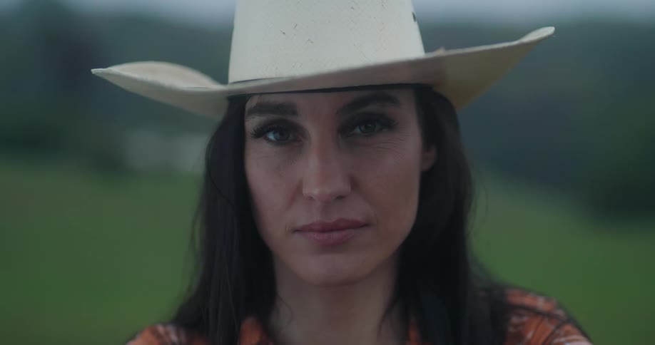 Woman in a cowboy hat looking into the camera at dusk or dawn
