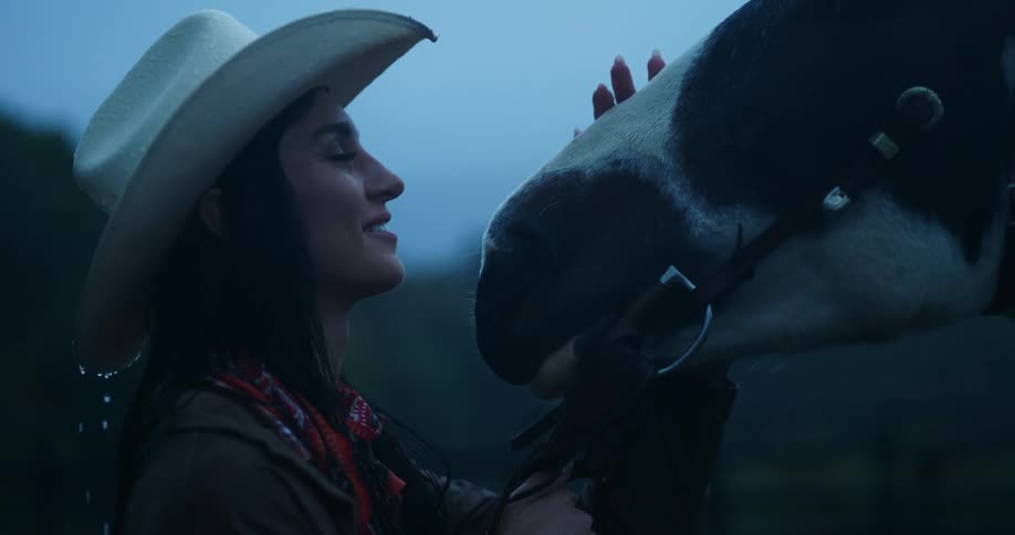 Cowgirl facing her horse in the rain with a felicitous facial expression