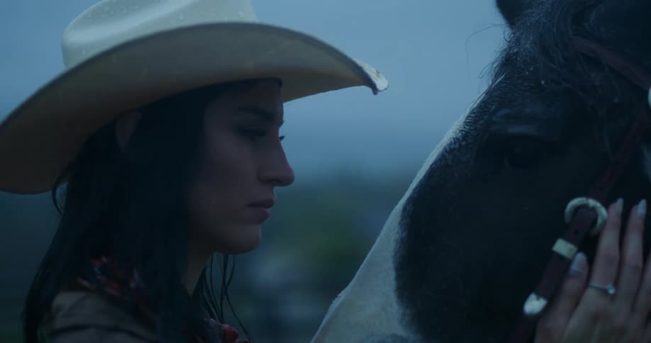 A cowgirl gazes fondly at her horse while stroking its cheek
