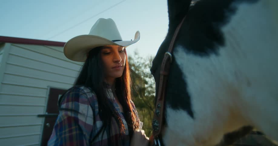 A woman in a cowboy hat is stroking a horses head