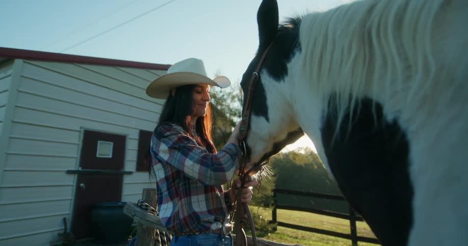 Woman wearing a cowboy hat tenderly stroking the horses face at a ranch on a sunny day