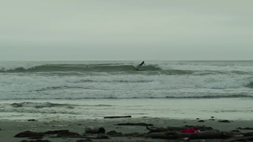 Surfer in the ocean with waves breaking under an overcast sky viewed from the shore