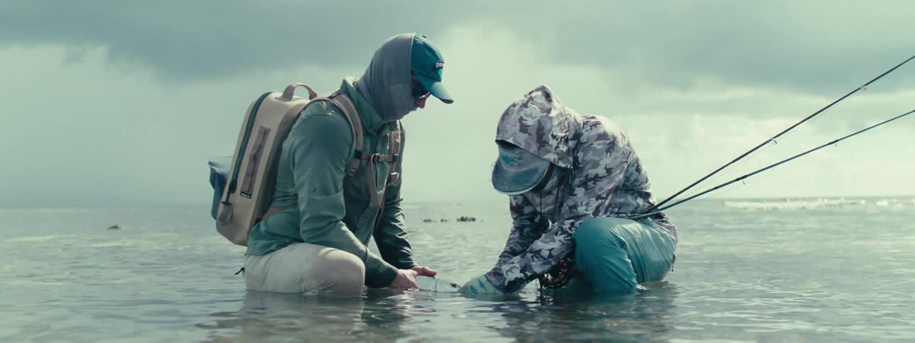 Two men crouching in the sea helping a fish