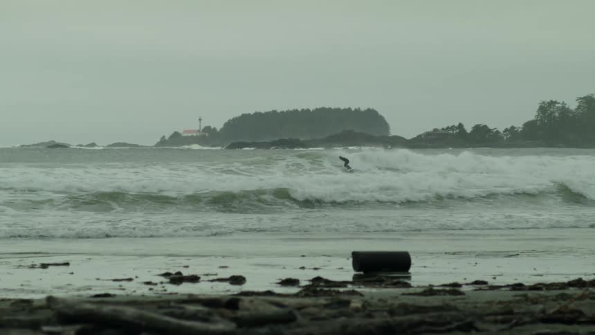 Surfer rides waves next to the coast on an overcast day