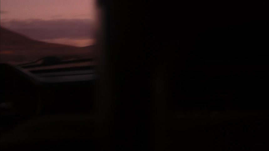 Woman driving a car in the middle of a natural road with a reddish dawn sky