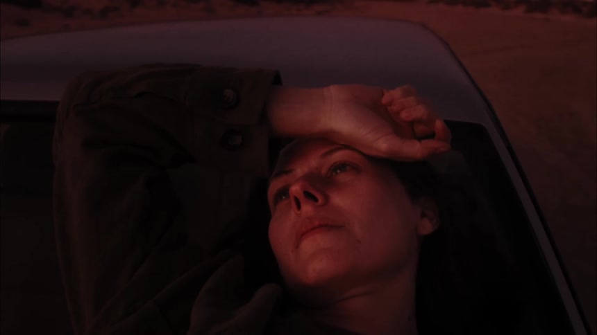 Introspective woman lying on the car hood and windshield deep in thought rubbing her hand on her head