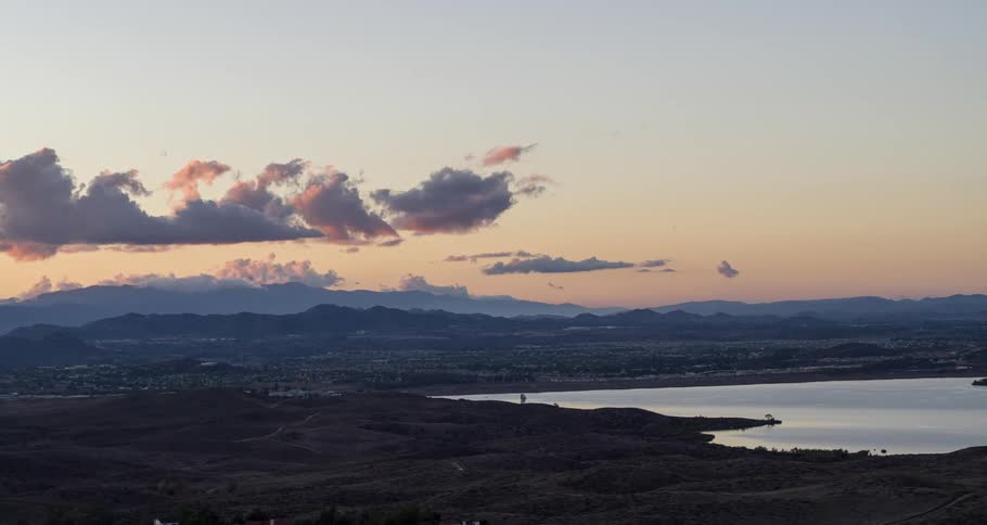 A city sits between a lake and a mountain range at sunrise