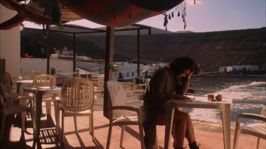 A woman is sitting and reading something in front of the sea and is distressed