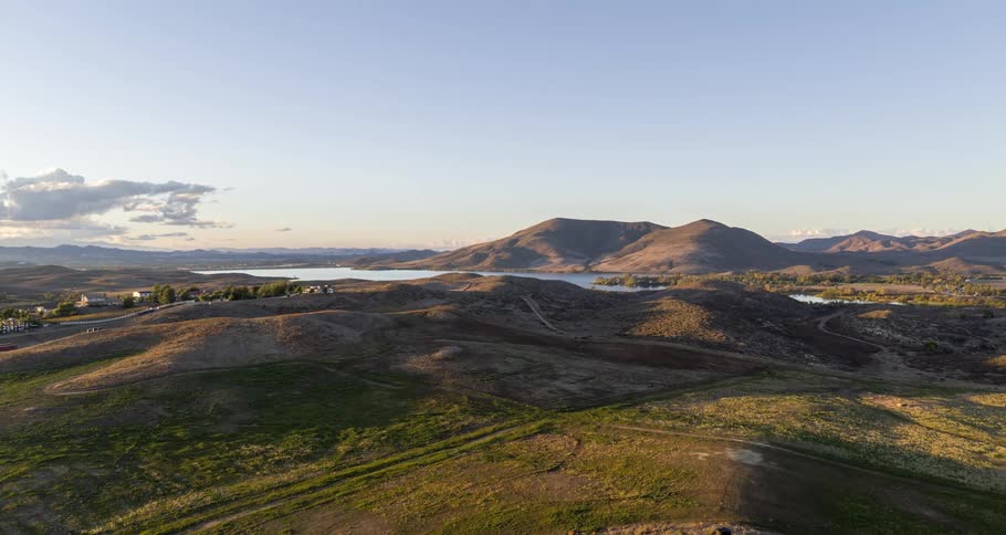 Aerial panorama of a highway next to a grassland mountain range and a lake in a morning sky