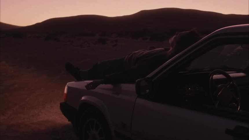 A person lying on the hood of the car observing the desert landscape