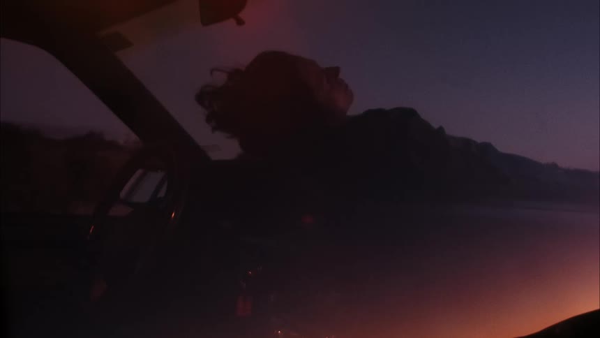 A woman lying on the hood of the car at night