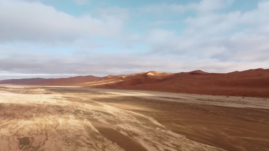 Desert salt bed next to large red hills under a blue sky with some clouds