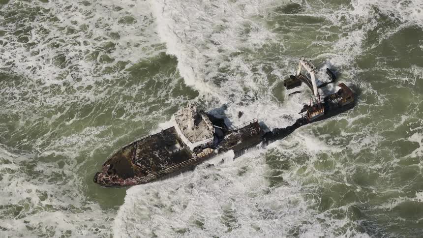 An aerial perspective capturing a shipwreck aground amidst the relentless ocean waves