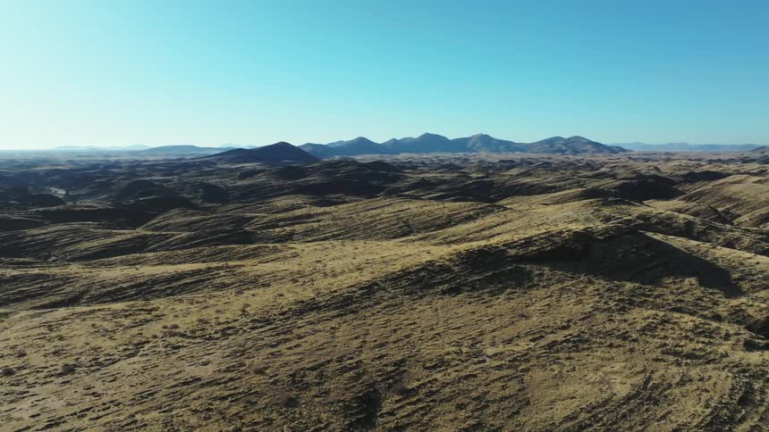 An aerial view of a field with several hills and mountains in the background