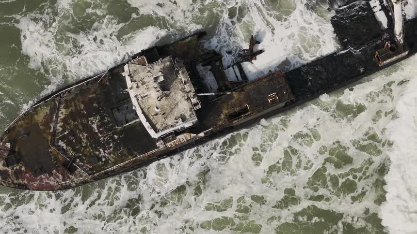 Aerial view of a shipwreck aground amidst the relentless ocean waves