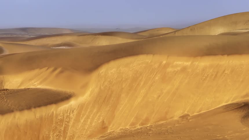 Desert sand shines golden under a hazy overcast sky