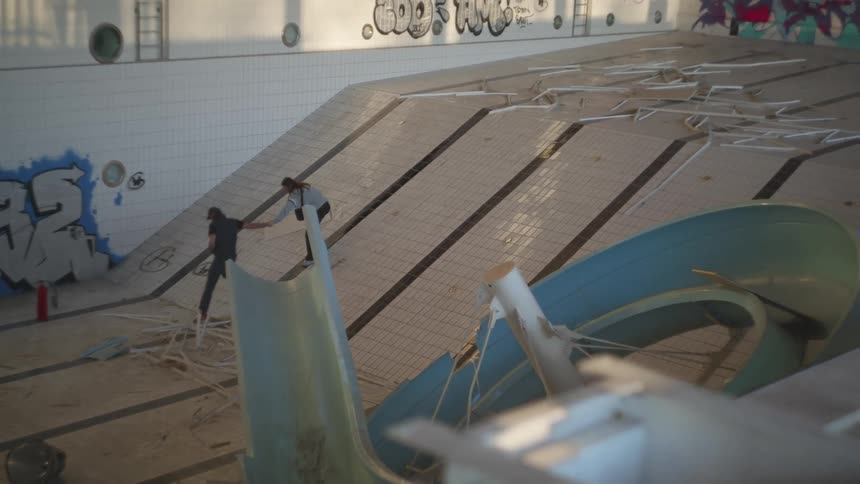 Two people going down into a huge swimming pool that has no water