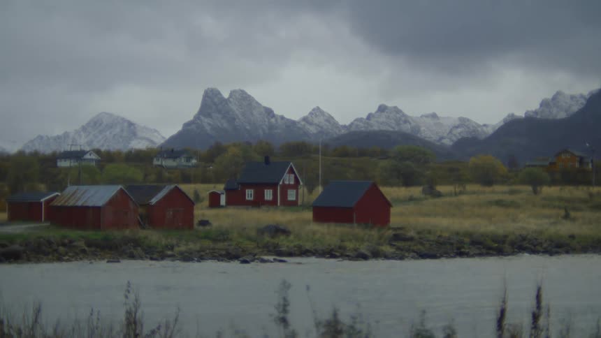 Road passes between red buildings situated near river and through autumnal woodsbordering mountains