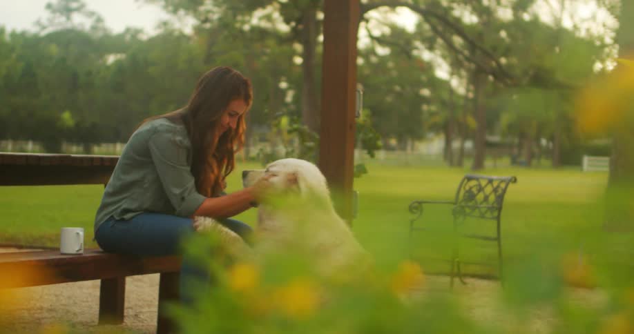 Lady rubs her dogs head while seated on a park bench during the day