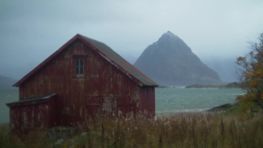 A wooden cabin on the beach with mountains as a backdrop