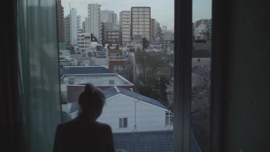 A woman watching the city from her bedroom window