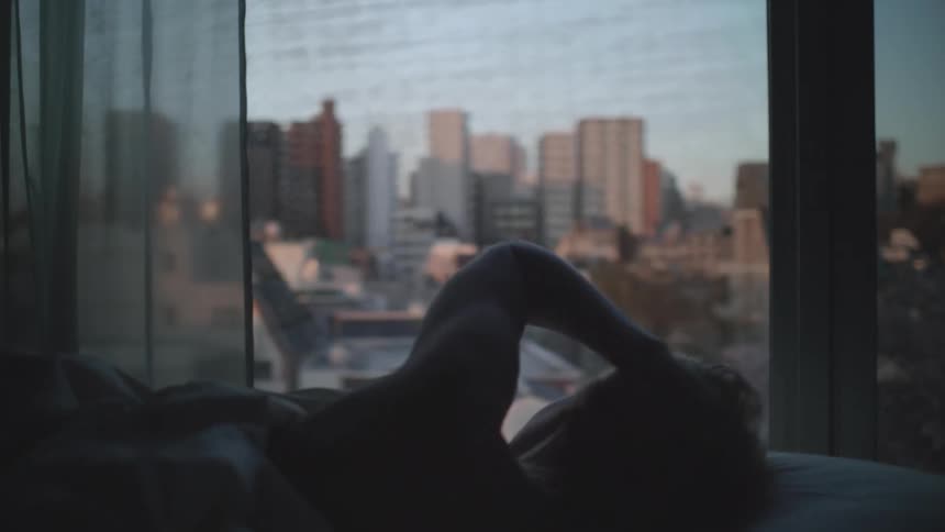 A woman lying in bed watching the city through the window